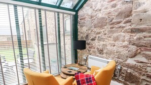 A room with a stone wall, a round wooden table with a lamp, and two yellow chairs.