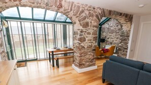 A spacious room with a stone wall, wooden flooring, a dining table set with plates and glasses, a sofa, and a view through large windows.