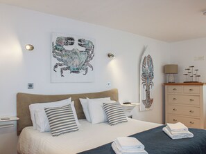 Una camera da letto ordinata con un letto, cuscini, una cassettiera e decorazioni alle pareti.