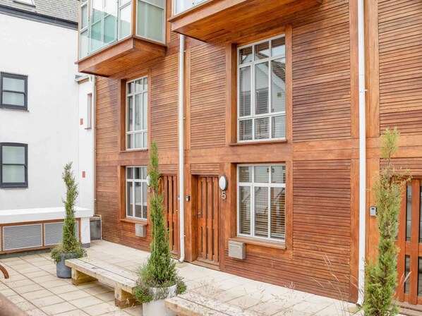 Un edificio a più piani con rivestimenti in legno, ampie finestre e una piccola zona esterna con fioriere.
