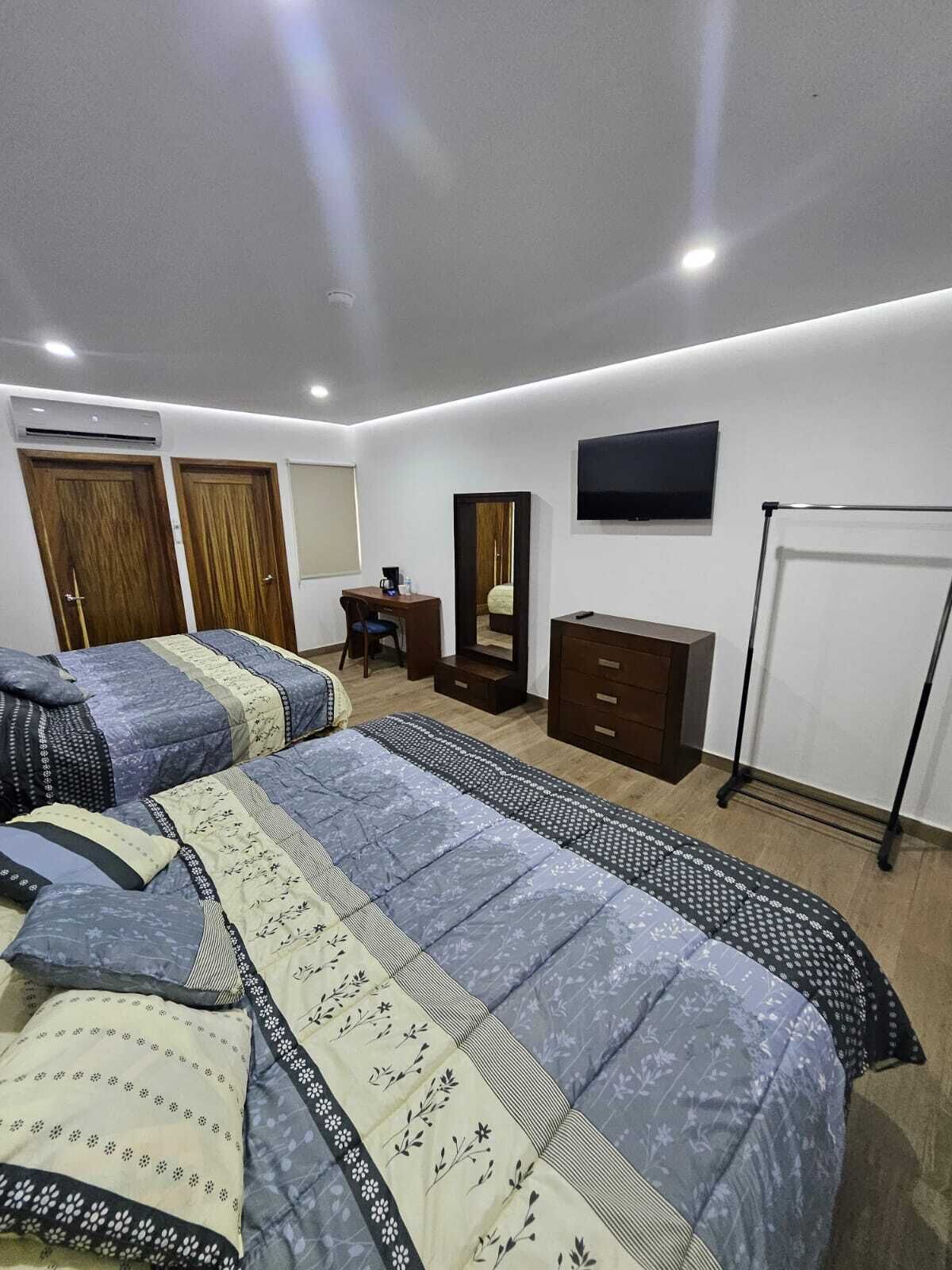 A modern hotel room with two beds, a desk, a dresser, a TV, and a wardrobe.