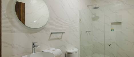 Un baño moderno con un lavamanos ovalado grande, un espejo redondo, ducha con cerramiento de vidrio y un inodoro.