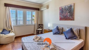 Una habitación de hotel con una cama, una silla, una mesita de noche y un ventanal con cortinas.