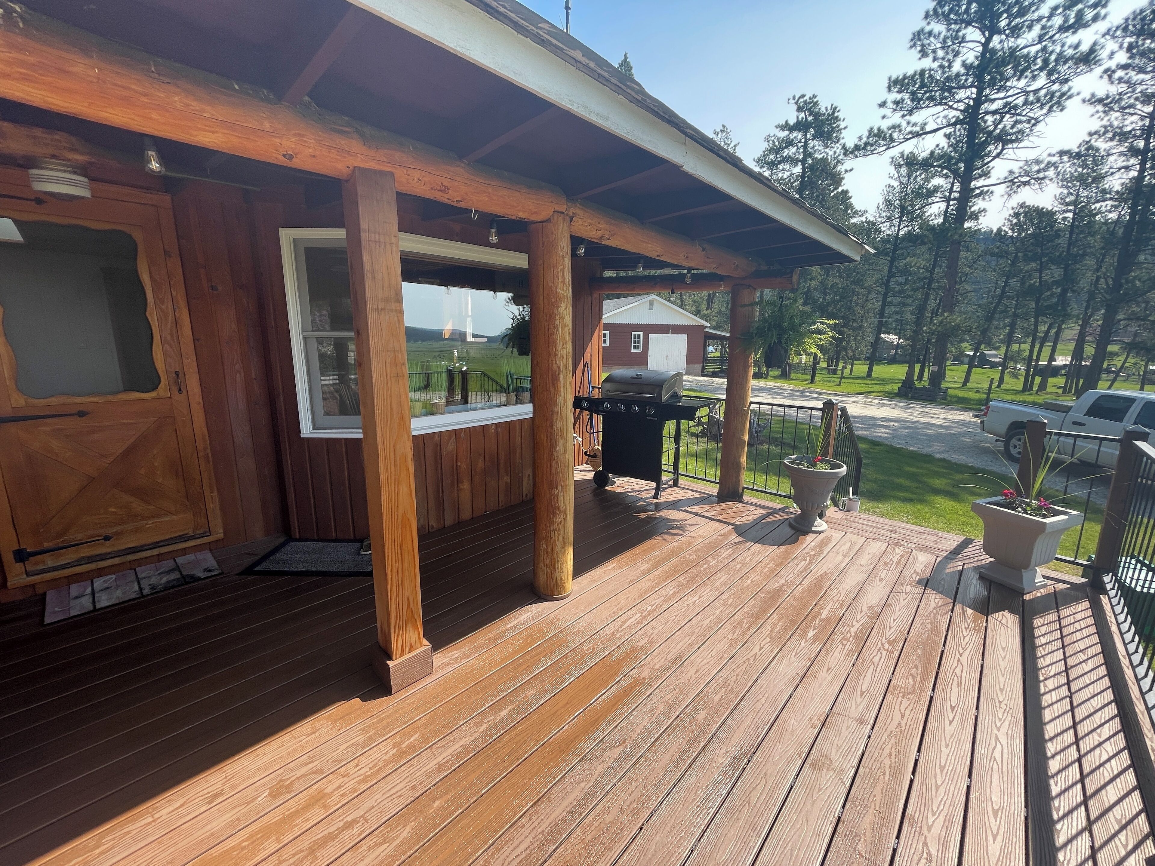 A wooden deck with a covered patio area, a grill, and a view of a residential area with trees and a house.