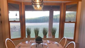 Una mesa de madera para comer con seis sillas, rodeada de ventanas que dan a un lago y un bosque.