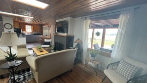 Una sala de estar acogedora con un sofá, una mesita y un televisor. Se observa una cocina al fondo, con armarios de madera y una zona de comedor.
