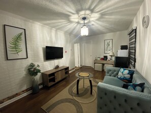A living room with a flat-screen TV, a wooden entertainment unit, a blue sofa, and a patterned rug.