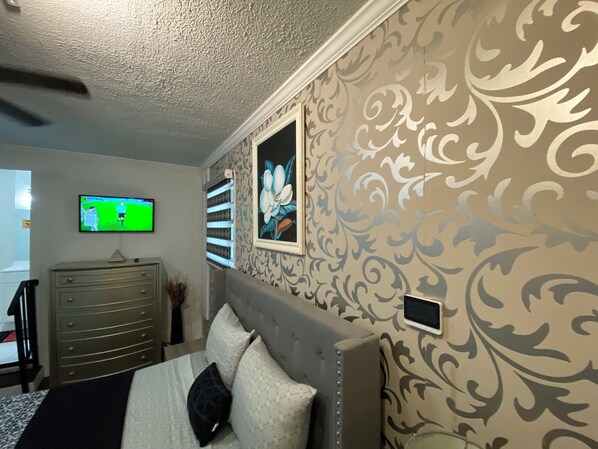 A bedroom with a bed, a dresser, a television mounted on the wall, and decorative wallpaper.