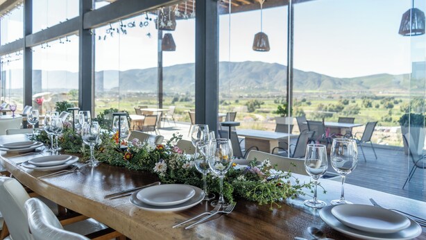 Mesa de jantar posta com pratos, copos e talheres, com vista para uma paisagem deslumbrante.