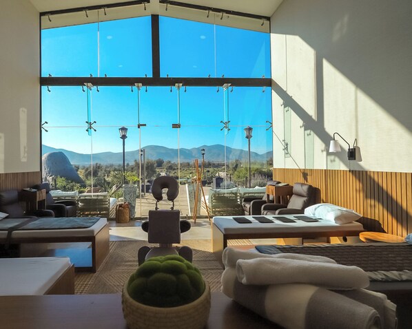 A modern room with a large window, a massage chair, a massage table, and a view of mountains.
