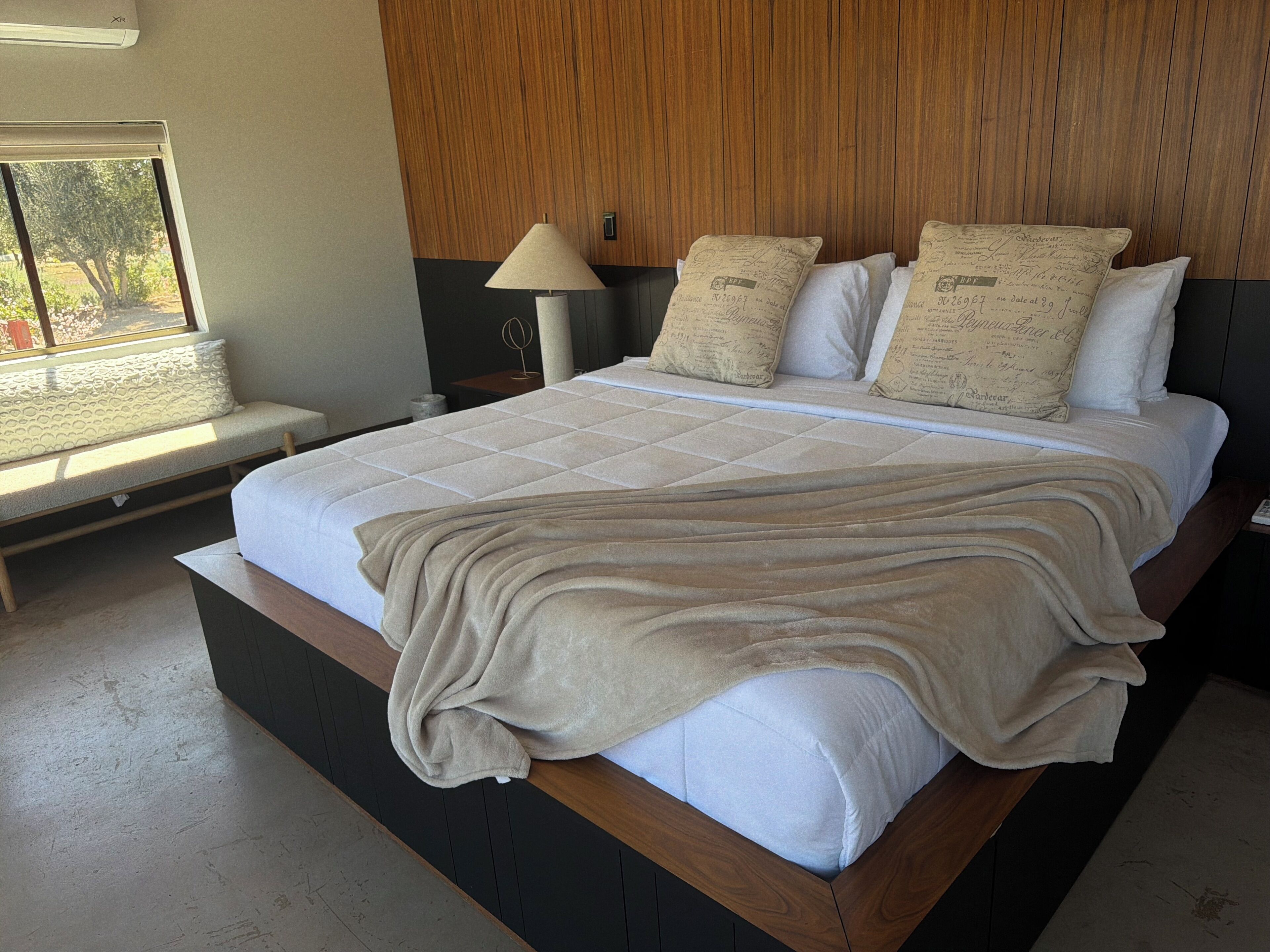 Un dormitorio con una cama grande, un banco junto a la ventana y una lámpara.