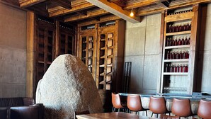 Interior de restaurante com uma grande peça central de pedra, vigas de madeira no teto e uma adega.