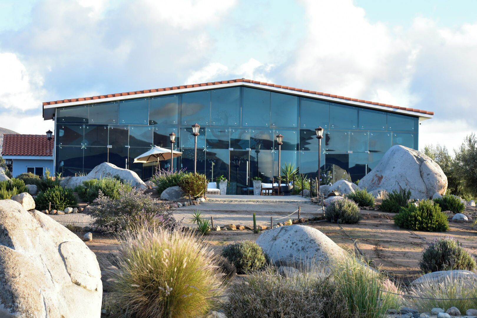 Un edificio moderno con fachada de vidrio, rocas grandes y mesas al aire libre.