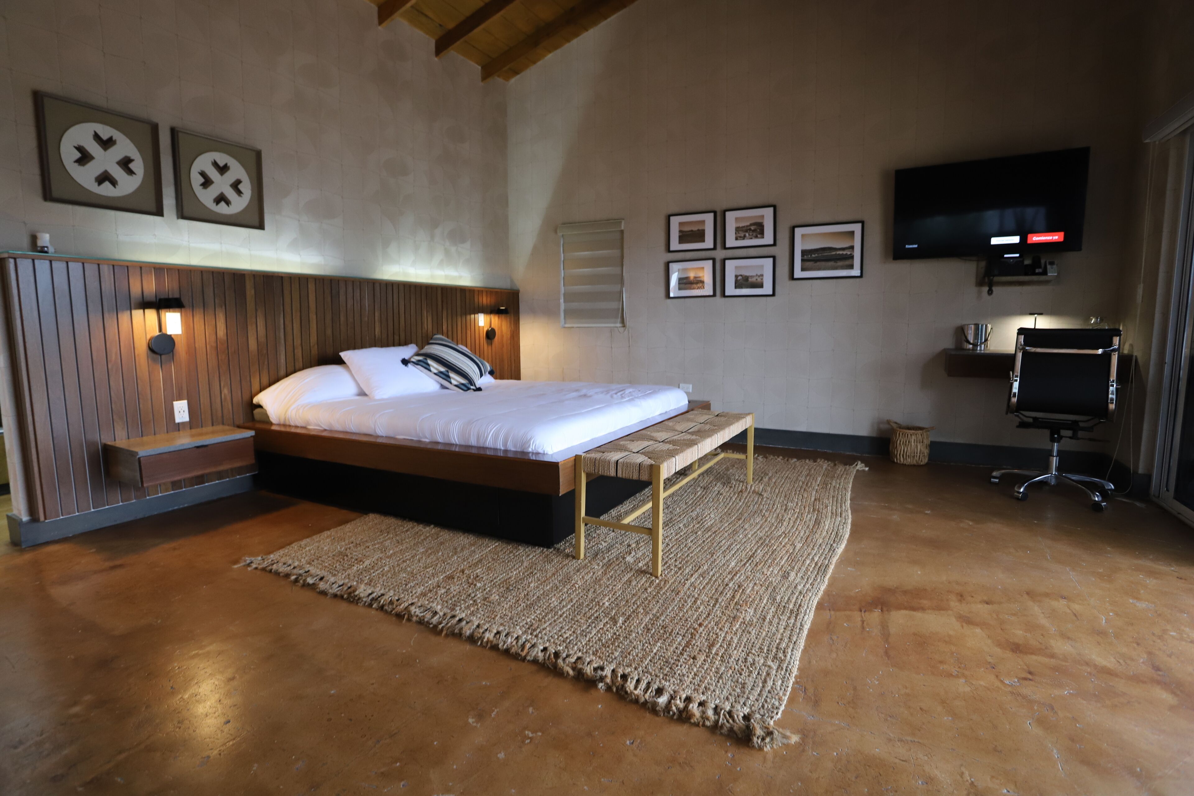 A bedroom with a bed, bedside table, wall-mounted TV, and framed pictures.