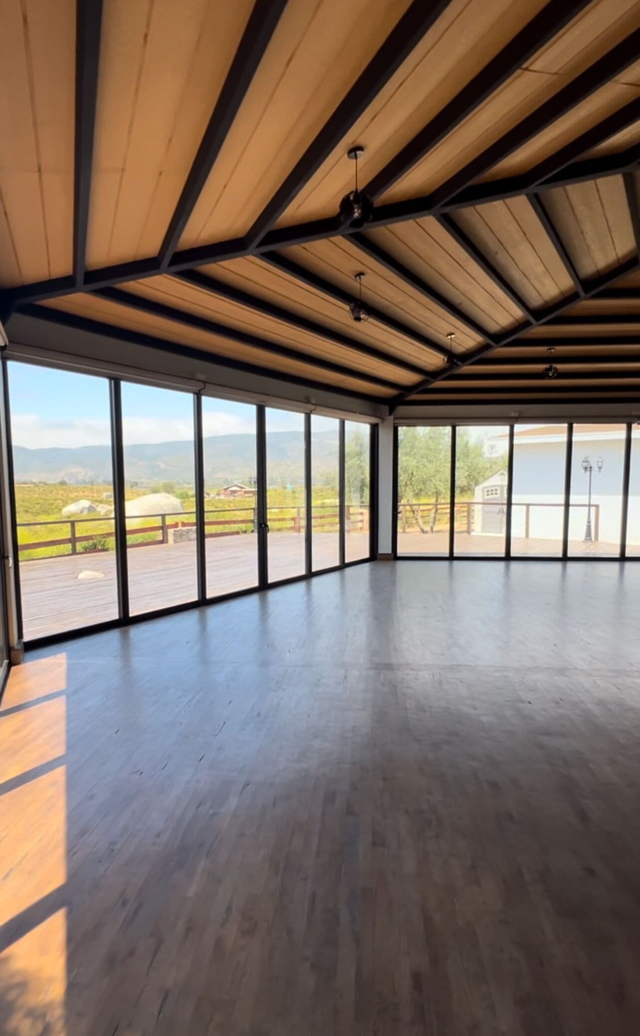 A spacious room with a high ceiling and large windows offering a view of a mountainous landscape.
