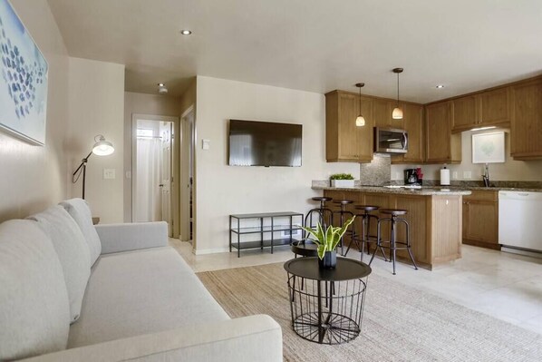 A modern kitchen with wooden cabinets, a central island, bar stools, and a flat-screen TV.