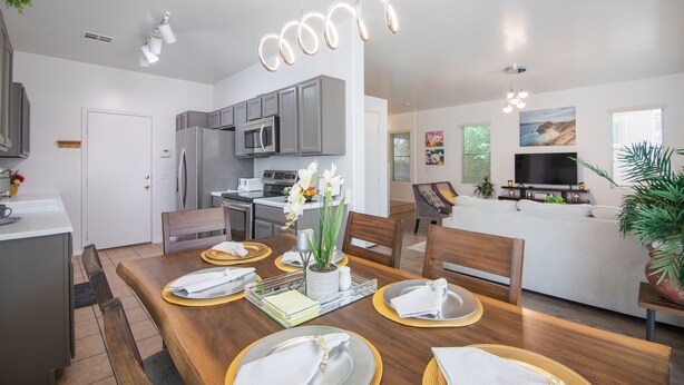 A modern kitchen with grey cabinets, a stainless steel refrigerator, and a microwave. There is a dining table set with plates, napkins, and a vase with flowers. - Stylish Vacation Home Phoenix - Low Rates NOW! (Phoenix)