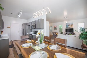 Une cuisine moderne avec des meubles gris, un réfrigérateur en acier inoxydable et un four à micro-ondes. On y trouve une table à manger dressée avec des assiettes, des serviettes et un vase rempli de fleurs.