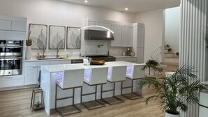 A modern kitchen with white cabinetry, stainless steel appliances, and a central island with bar stools. - Lake Paradise  (Six Mile)