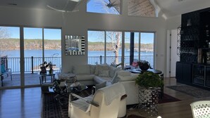 A spacious living room with a large window overlooking a lake, a ceiling fan, and a modern kitchen area. - Lake Paradise  (Six Mile)