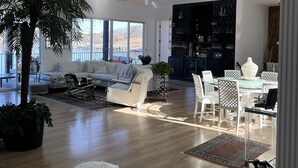 A spacious living area with a large white sofa, a dining table with chairs, a white fluffy rug, and a tall plant. - Lake Paradise  (Six Mile)