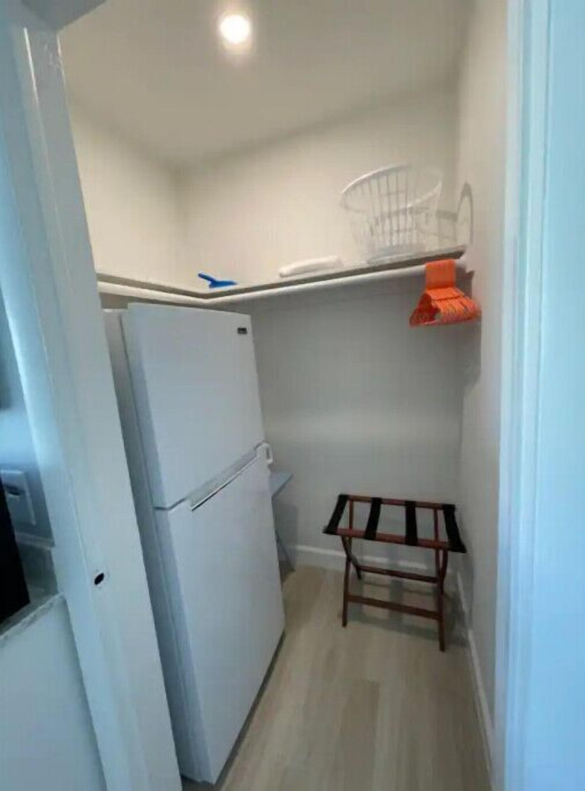 Ett litet kök med ett vitt kylskåp, en träpall och en vit hylla med en korg.