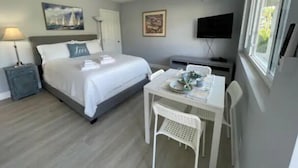 Et hotelværelse med seng, skrivebord med stol, fjernsyn og et vindue.