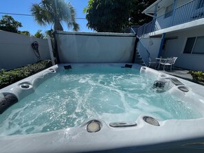 A hot tub with a control panel, surrounded by a white wall, a blue railing, and a small patio area with chairs. - Hot Tub, Walk to Beach, Snorkeling, Surfing (Riviera Beach)