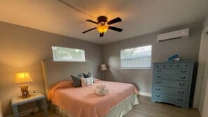 A bedroom with a bed, a nightstand, a dresser, a ceiling fan, and two windows. - Hot Tub, Walk to Beach, Snorkeling, Surfing (Riviera Beach)