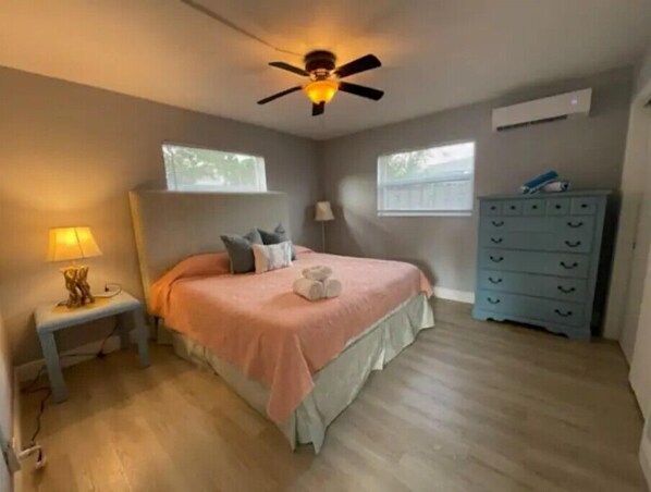 A bedroom with a bed, a nightstand, a dresser, a ceiling fan, and two windows. - Hot Tub, Walk to Beach, Snorkeling, Surfing (Riviera Beach)