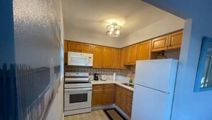 A compact kitchen with wooden cabinets, a white refrigerator, a microwave, and a stove. - Hot Tub, Walk to Beach, Snorkeling, Surfing (Riviera Beach)