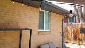 Un espacio de estar al aire libre cubierto con pared de ladrillo, un sofá de mimbre y una mesa de madera.