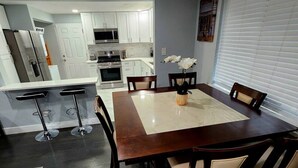 Un comedor con una mesa y sillas de madera, una cocina al fondo y una ventana con persianas.