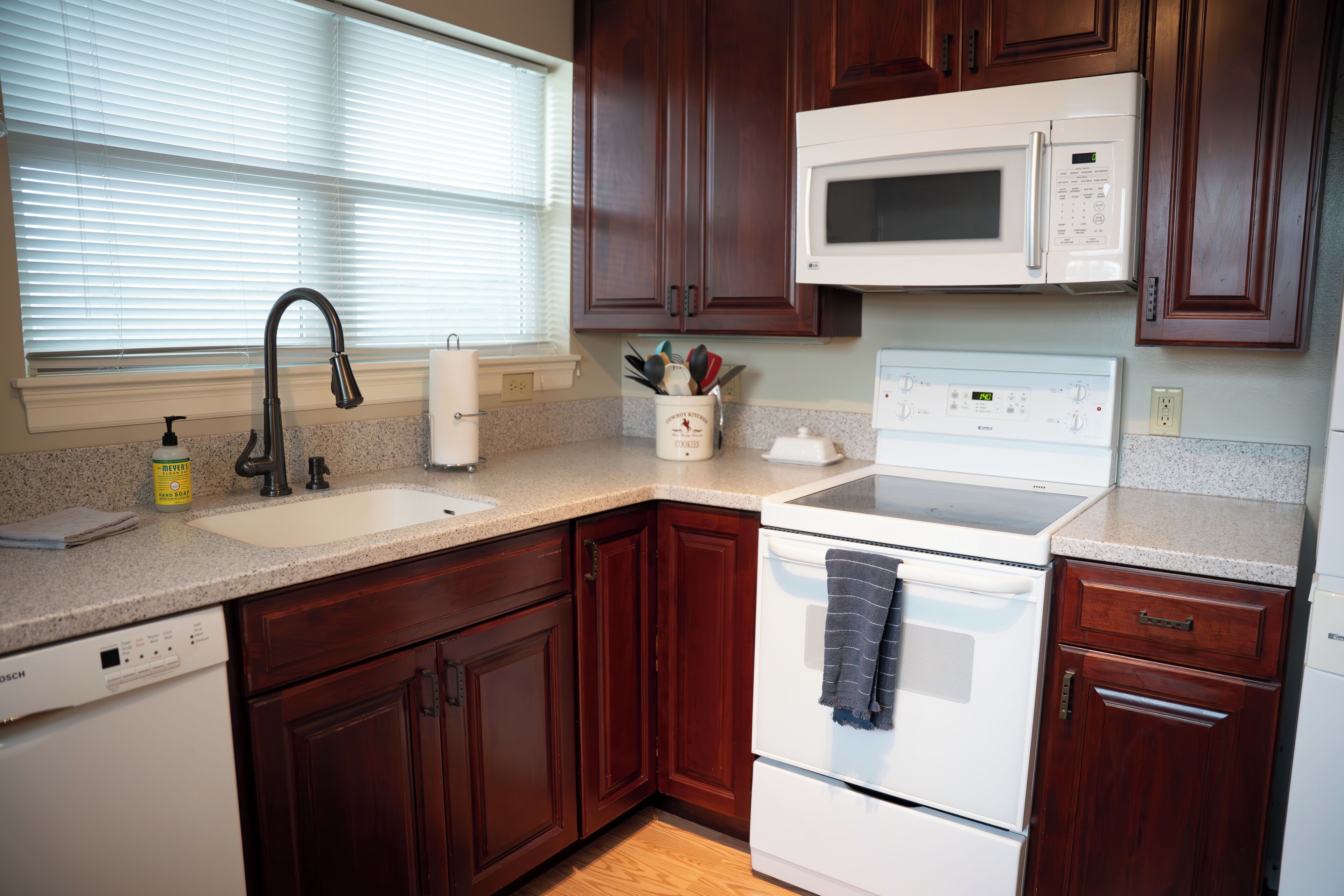 A kitchen with wooden cabinets, a white dishwasher, a microwave, and a stove.