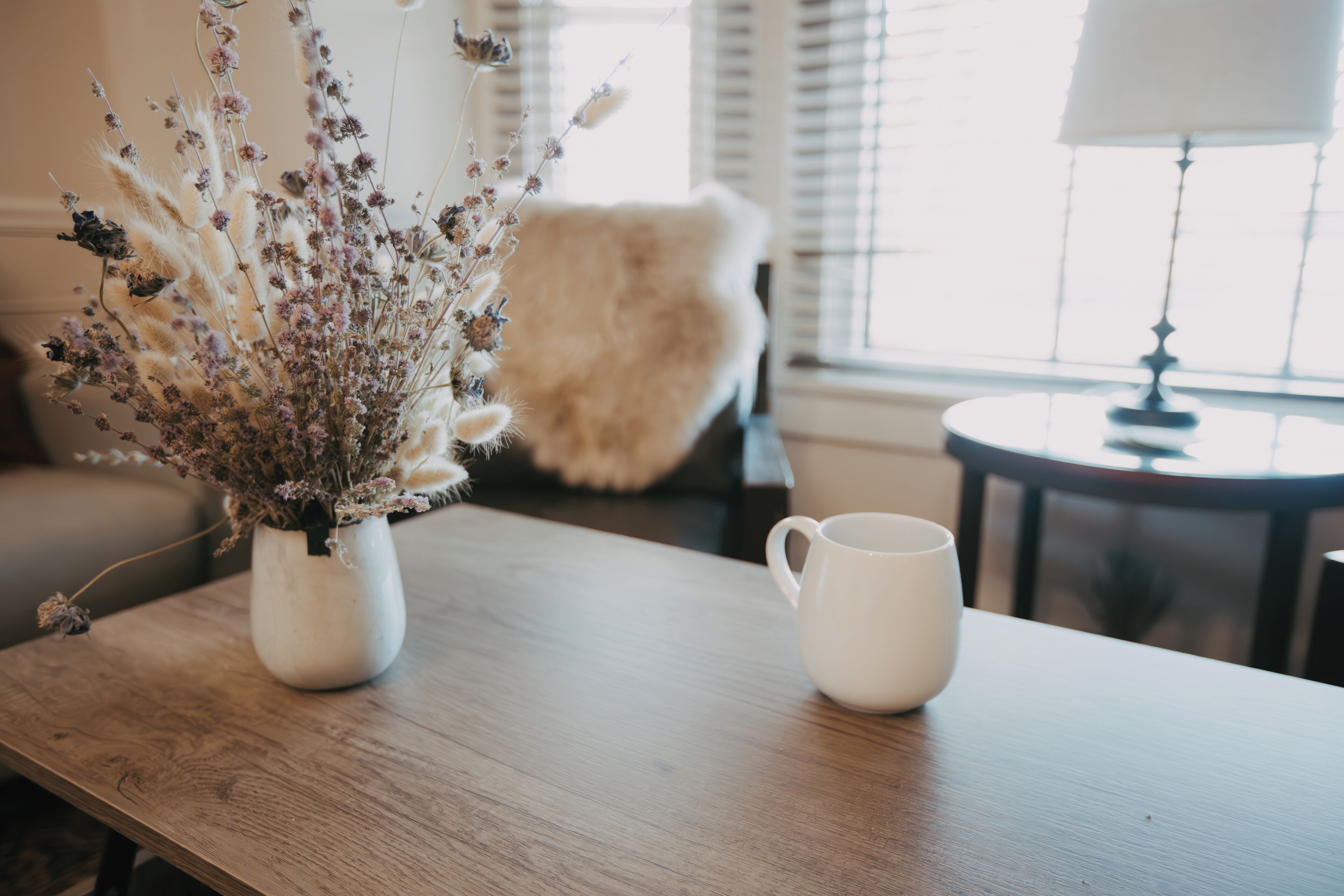 A wooden table with a white vase of dried flowers and a white mug.