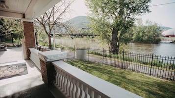Un'area esterna coperta con un muro in mattoni, una ringhiera metallica e vista su un fiume con un ponte e alberi.