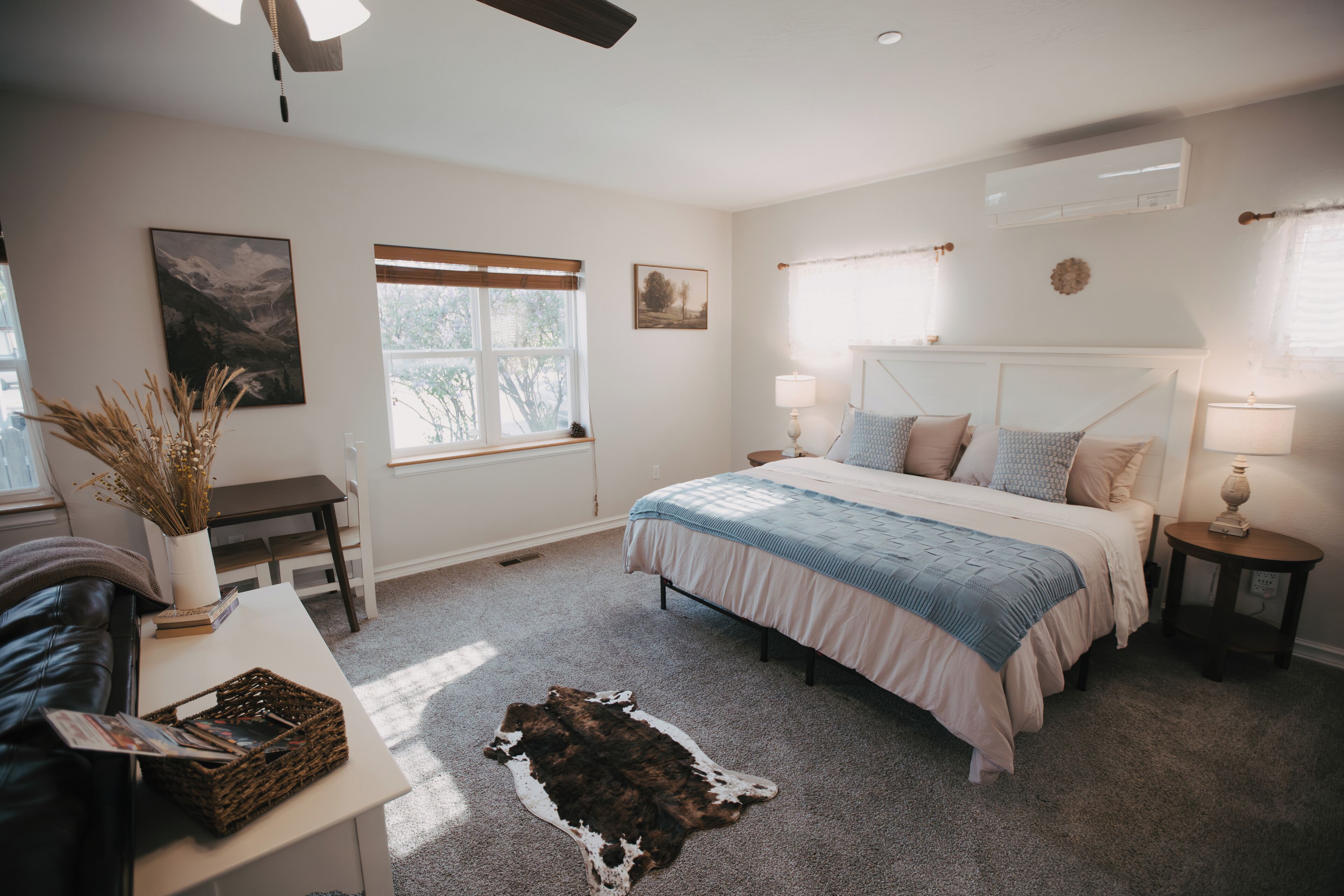 Quarto com uma cama, mesas de cabeceira, escrivaninha e janela.