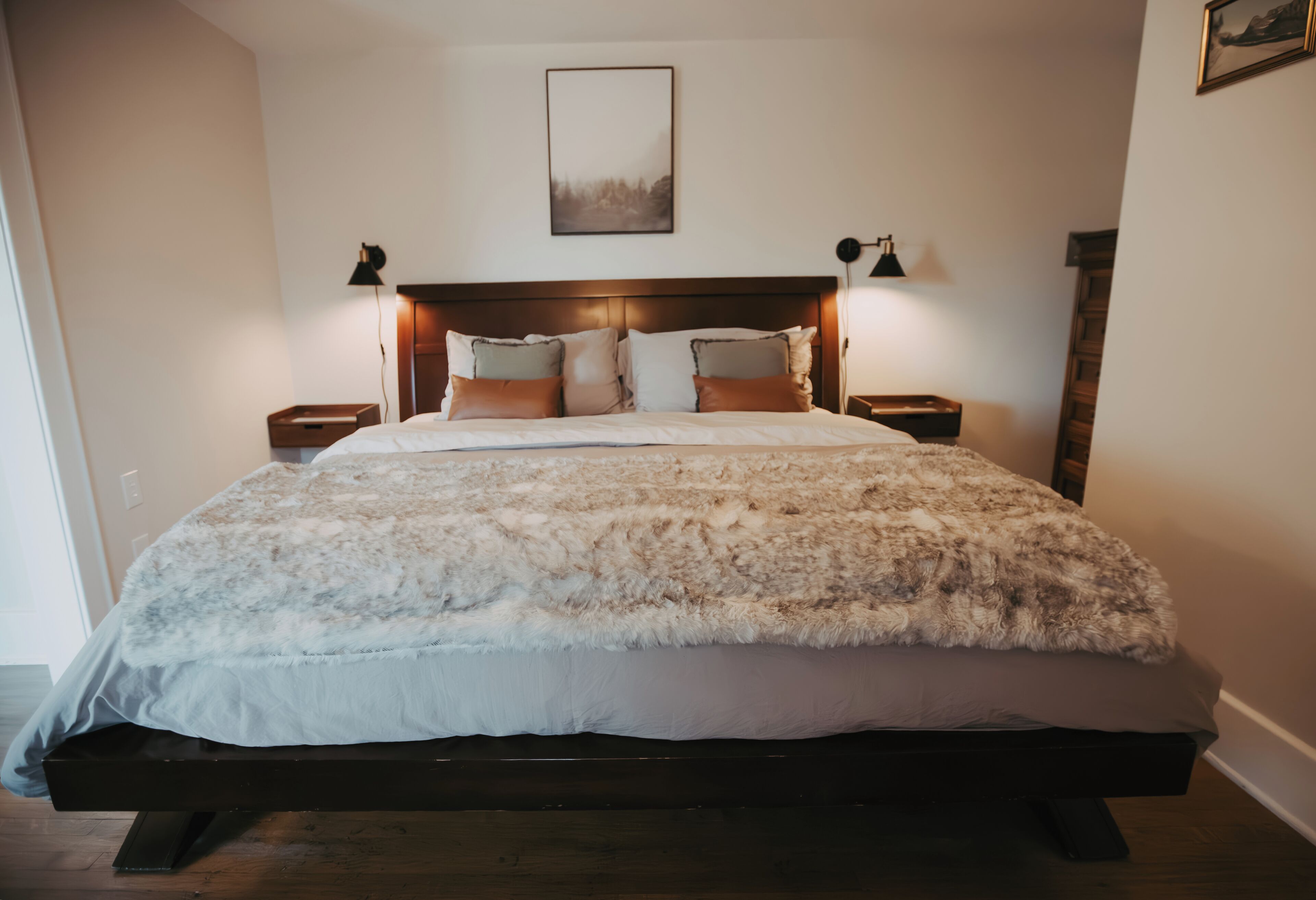 A large bed with a fluffy white and brown blanket, two bedside lamps, and a framed picture on the wall.