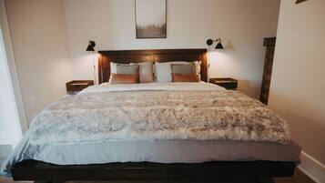 A large bed with a fluffy white and brown blanket, two bedside lamps, and a framed picture on the wall.