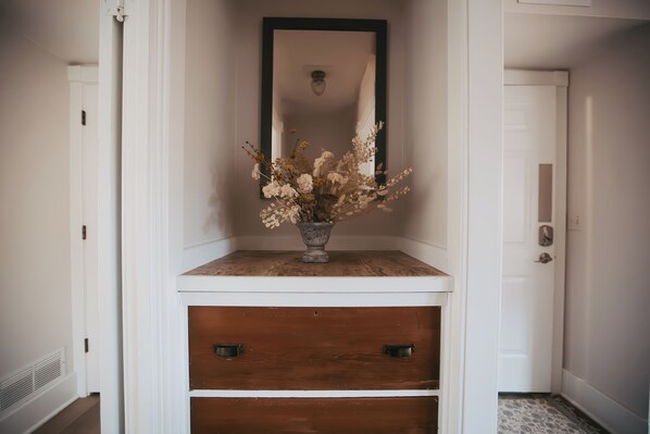 A hallway with a white console table topped with a vase of dried flowers, a mirror above it, and a white door on the right.