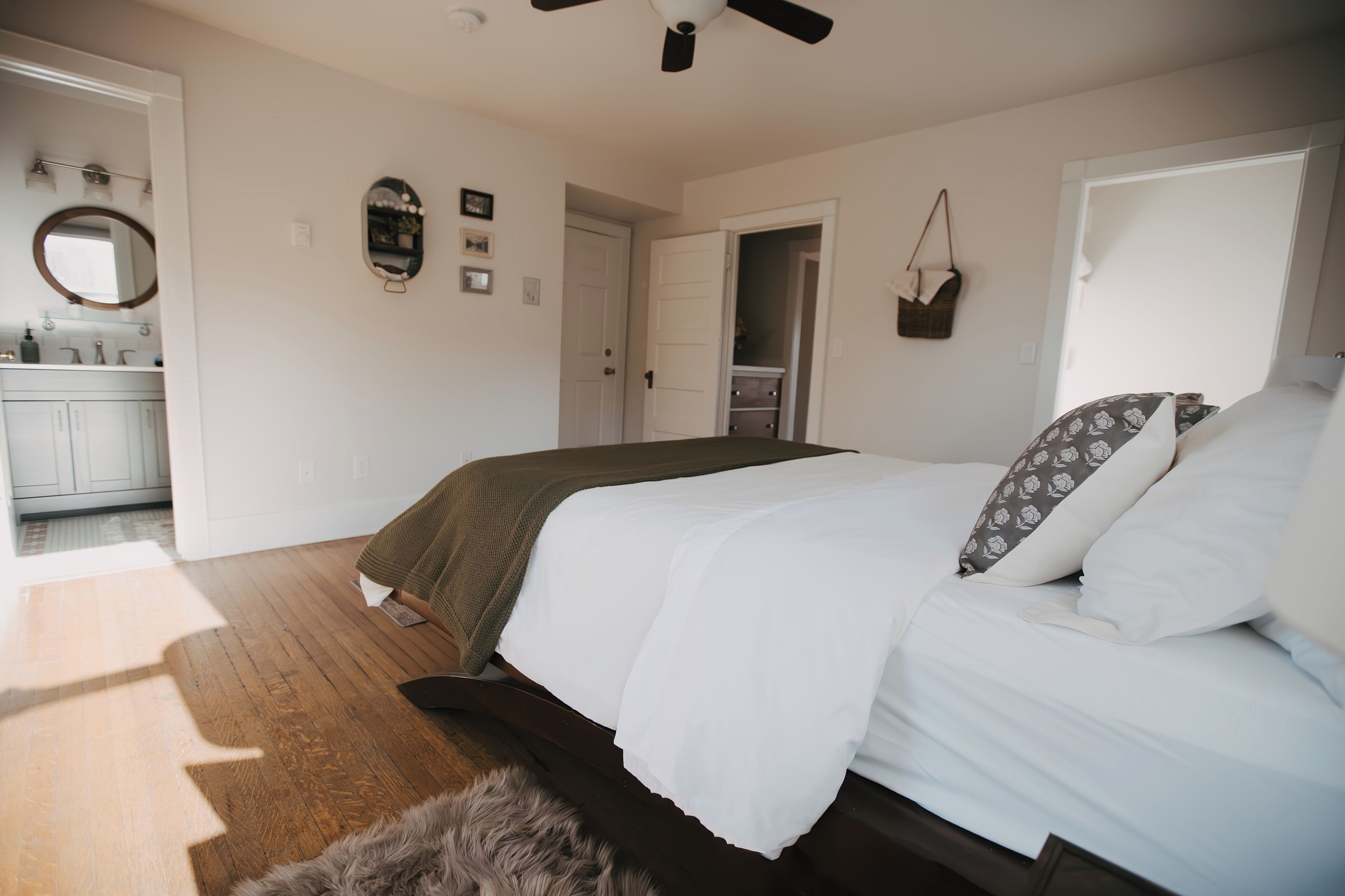 A bedroom with a bed, a ceiling fan, a door, and a bathroom visible in the background.