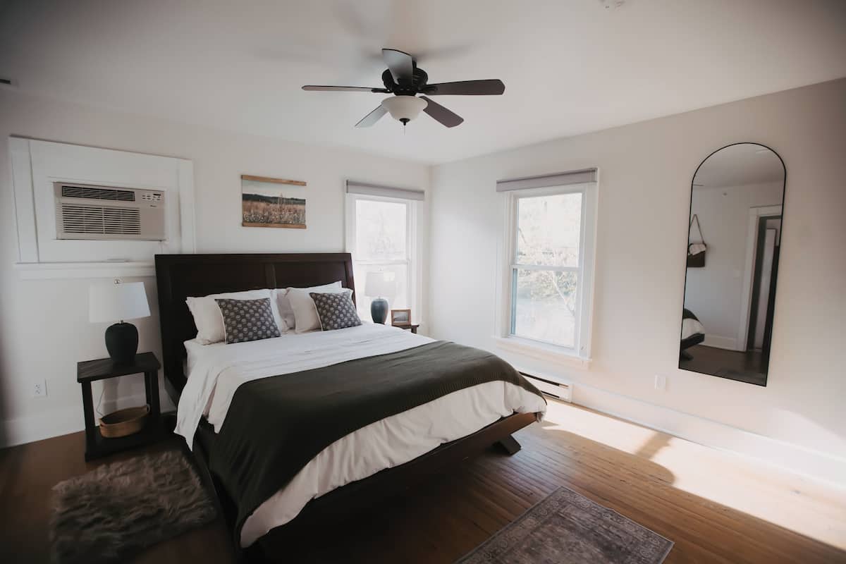 Un dormitorio con una cama grande, ventilador de techo, ventana y espejo.