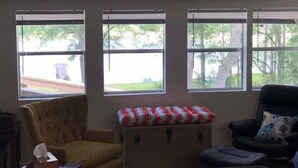 Una habitación con tres ventanas, un sillón amarillo, un sillón negro y una mesita con una caja de pañuelos.
