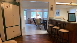 Una cocina con piso de madera, una barra con taburetes y una zona de comedor con sillas.