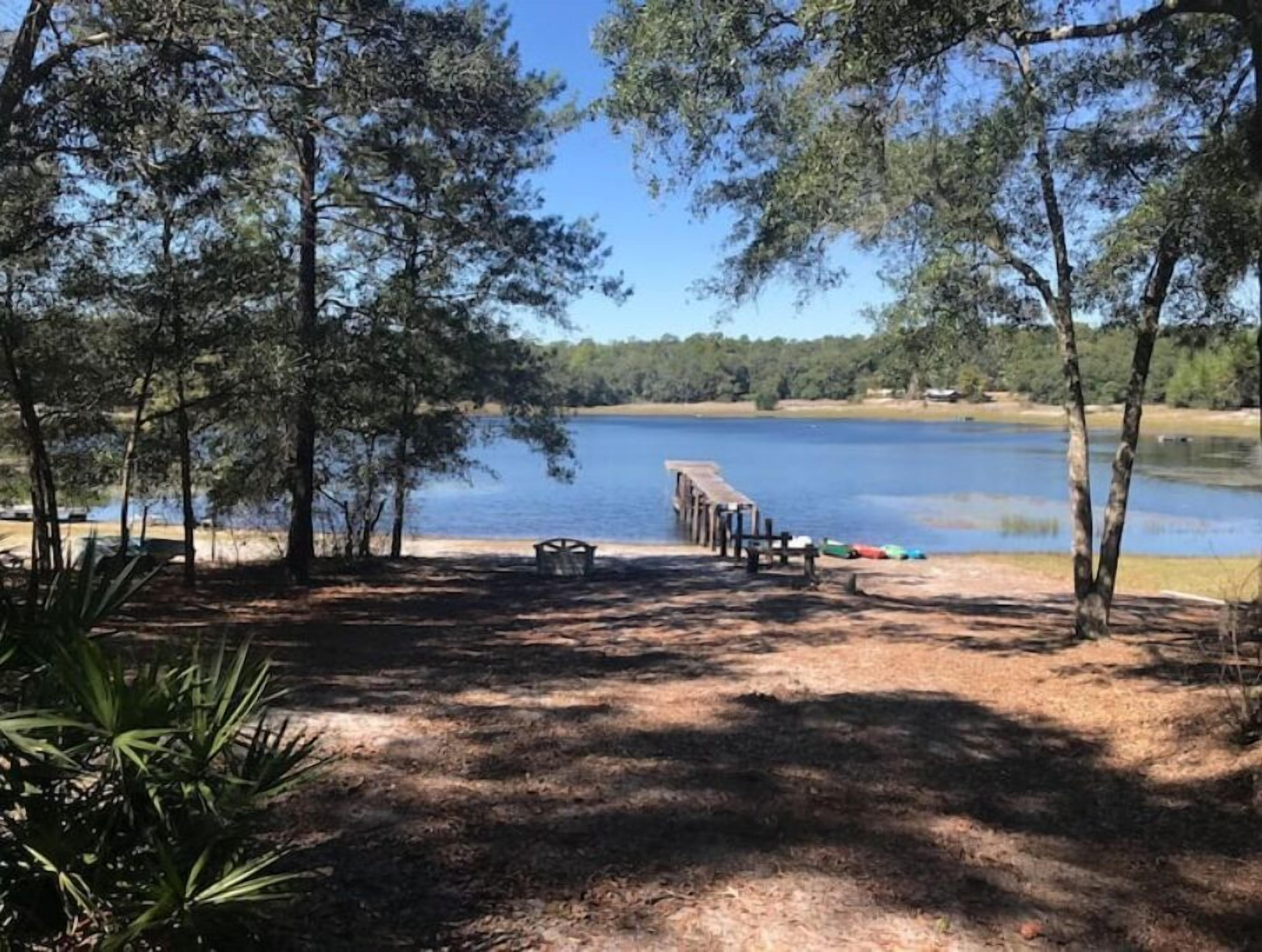 Campament a la vora d'un llac amb un moll de fusta que s'endinsa a l'aigua, envoltat d'arbres i un cel serè.