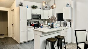 Una cocina moderna con armarios blancos, una isla central, taburetes de bar y una cafetera.