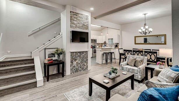 Una sala de estar moderna con una escalera, una cocina al fondo y un comedor con candelabro.