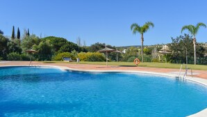 Una piscina con agua cristalina azul, rodeada de palmeras y una zona verde.