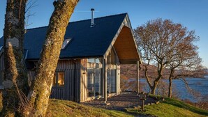 A modern house with a sloped roof, large glass windows, and a wooden exterior. - The View, Duisdale Mor,  Sleat (Isle of Skye)