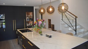 A modern kitchen with a large island, pendant lights, and a vase of flowers. - 4 Bedroom House in Sotogrande Alto (San Roque)